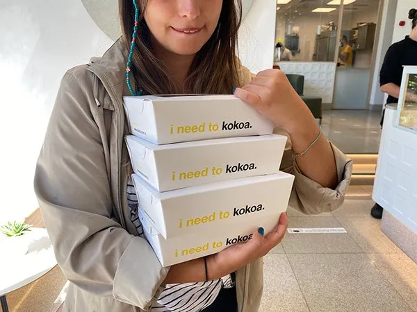 A customer holds a stack of white boxes printed 'i need to kokoa.'