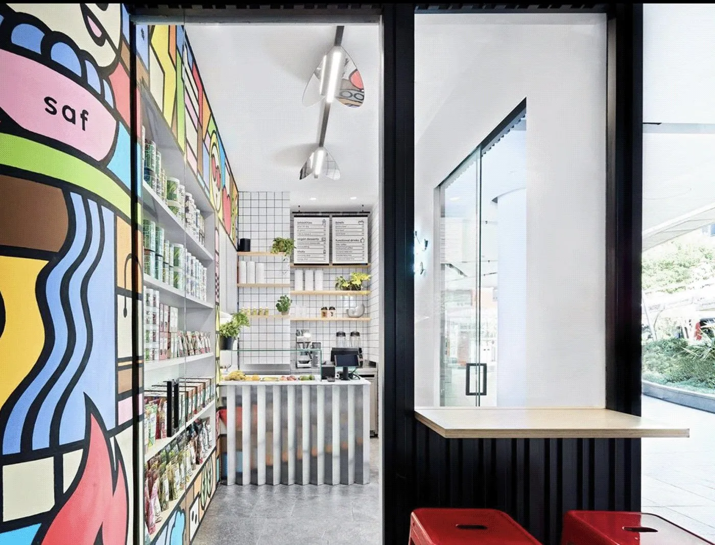 The store interior with the mural framing the window, a bench and red stools.