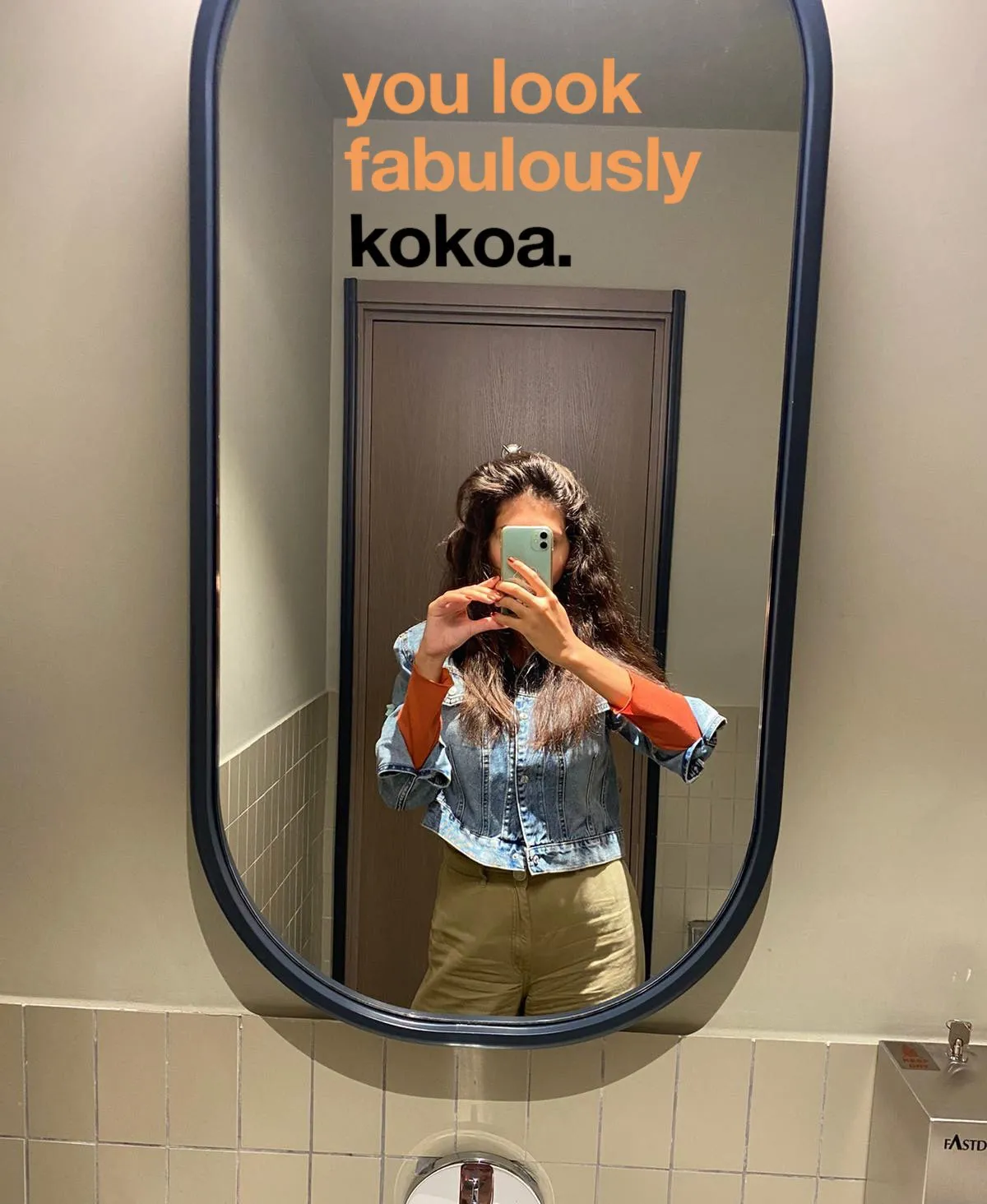 A mirror in the café printed with 'you look fabulously kokoa.' as a customer takes a photo.